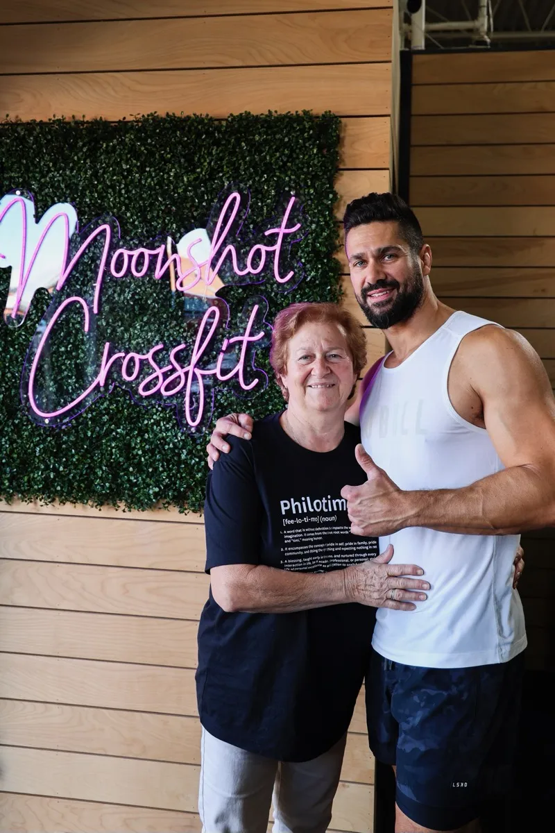 A coach and member posing together in front of the Moonshot CrossFit neon sign